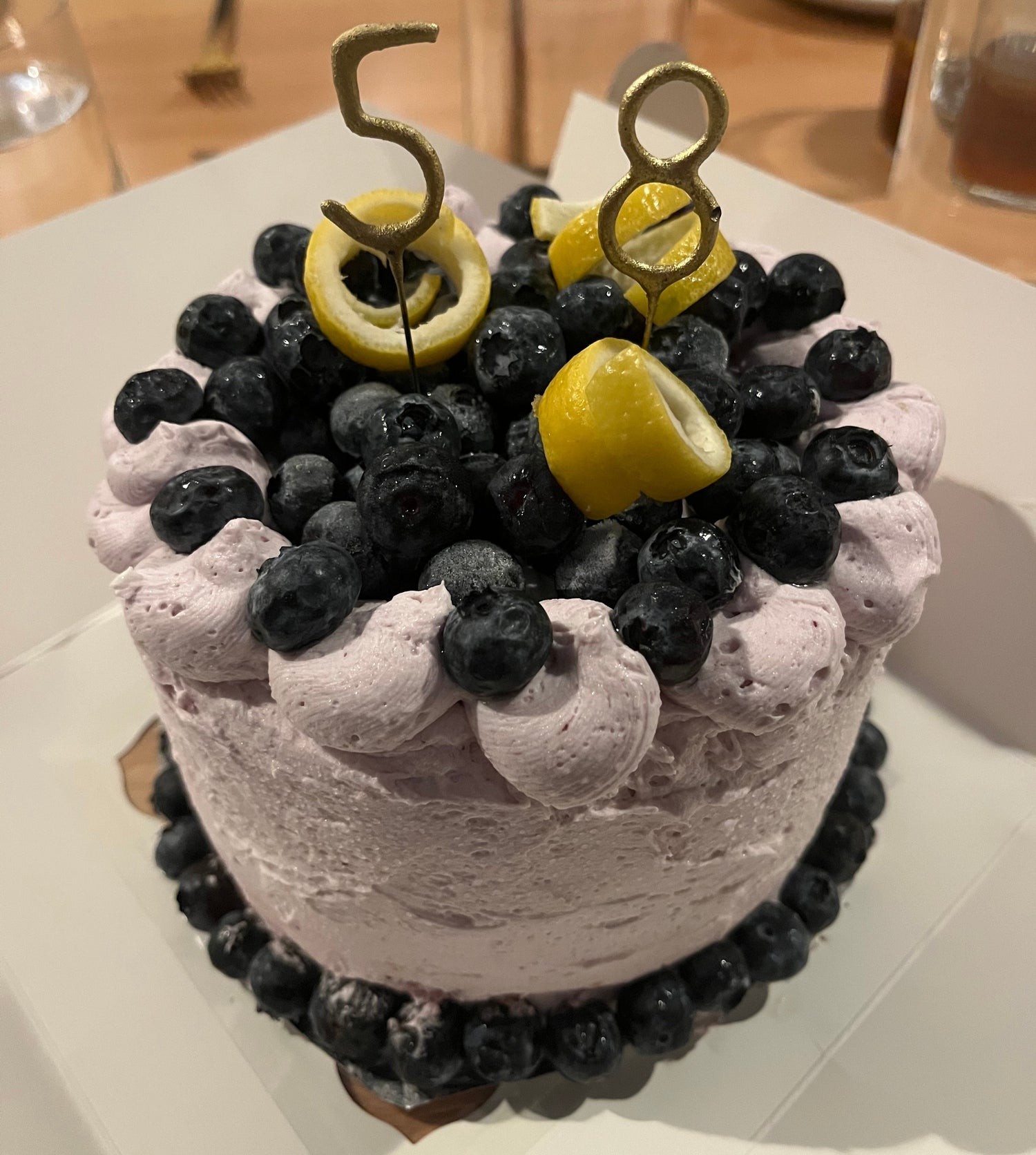 Birthday cake topped with fresh blueberries, lemon twists, and lavender-colored frosting
